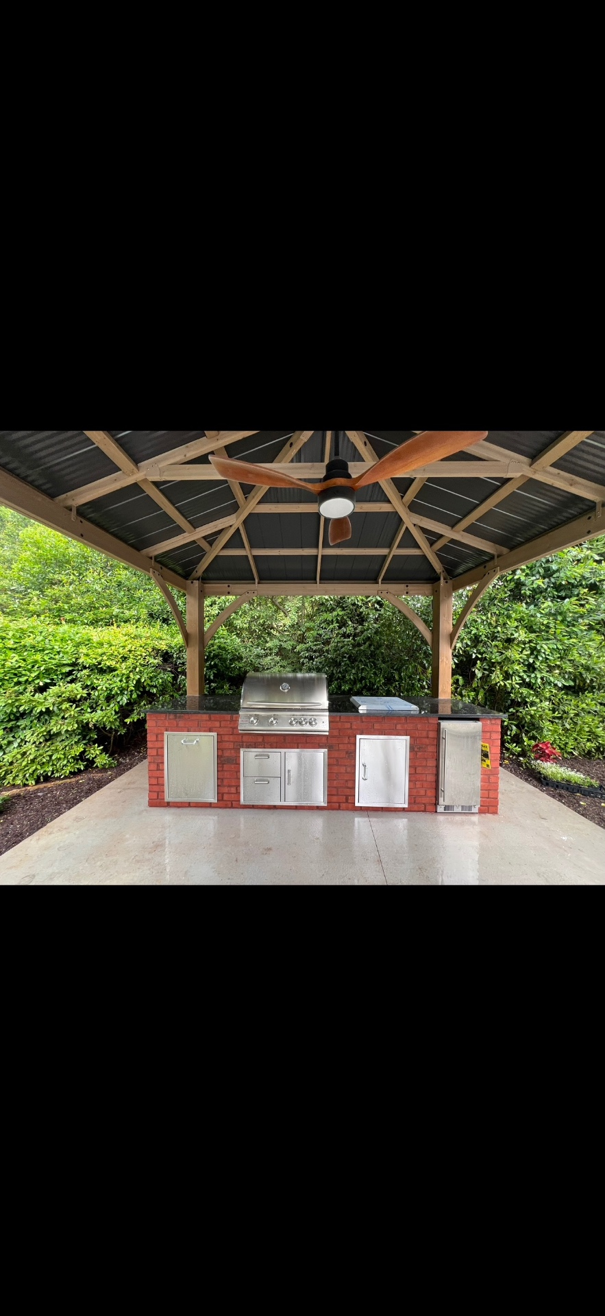 Outdoor kitchen with brick island, grill, and wood gazebo pavilion