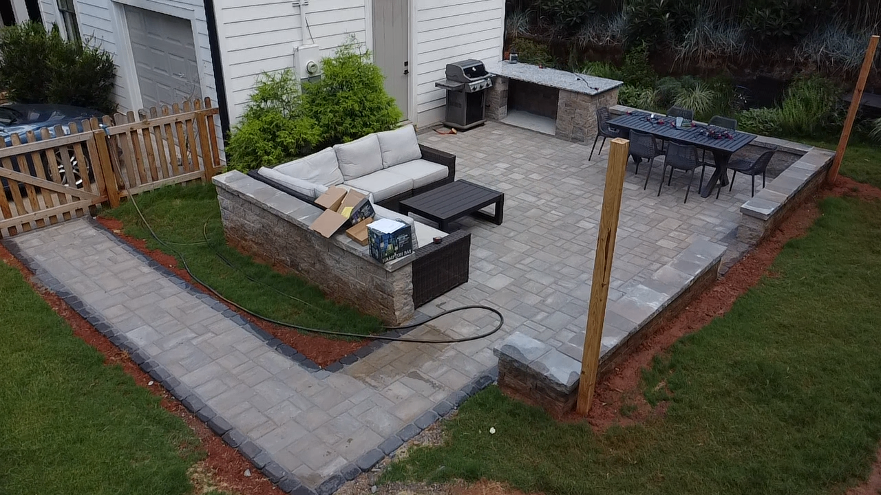 Angled aerial shot of a backyard paver patio with retaining seat wall and dining area